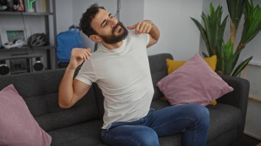 Modern bir oturma odasındaki kanepede uzanan sıradan giyinmiş yakışıklı sakallı adam..