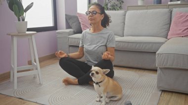 Yanında bir chihuahua otururken rahat bir dairede meditasyon yapan yetişkin bir kadın.