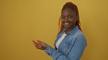 Gülümseyen Afrikalı bir kadın, parlak sarı bir arkaplan karşısında elini uzatıyor, günlük kot giyiyordu..