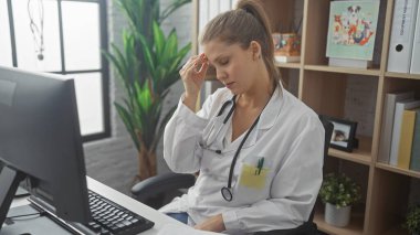 Steteskopu, bilgisayarı ve bitkileri olan, klinikte çalışan stresli bir kadın doktor sağlık sigortası senaryosu gösteriyor..