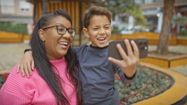 Gülümseyen bir kadın ve çocuk şehir parkında selfie çekiyorlar. Açık havada sevgi ve aile portresi çiziyorlar..