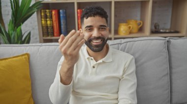 Gülümseyen genç İspanyol adam, kapalı bir koltukta oturan davetliyi işaret ediyor.