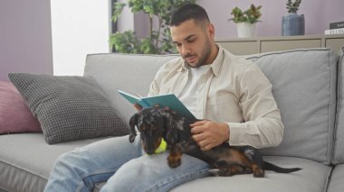 İspanyol adam rahat oturma odasındaki kanepede dachshund ile kitap okuyor.
