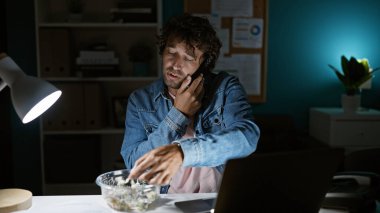 Genç bir İspanyol adam, loş bir ofiste telefonla konuşuyor, acil bir durum ve odaklanma hissi veriyor..