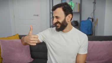 Modern bir dairede gülümseyen sakallı bir adam başparmağını kaldırıyor.