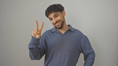 Sakallı neşeli genç bir adam beyaz bir geçmişe karşı barış işareti yapıyor.