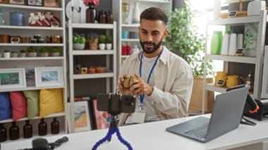 Sakallı genç İspanyol adam dekoratif eşyalarla dolu rafları olan bir mağazada içerik kaydediyor.