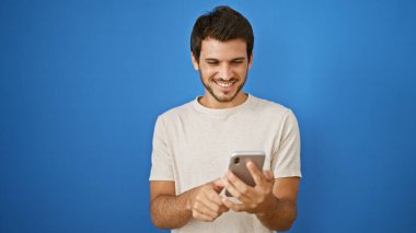 Yakışıklı, İspanyol asıllı, akıllı telefona gülümseyen açık hava duvarında izole edilmiş genç bir adam..
