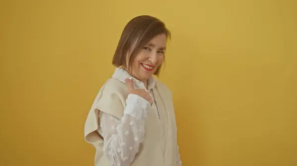 stock image A smiling middle-aged woman with short hair poses in a cream outfit against a yellow background, exuding confidence and joy.