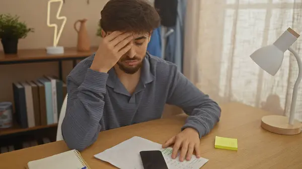 stock image A stressed young man with a beard at home looking at documents, suggesting financial worries or planning.