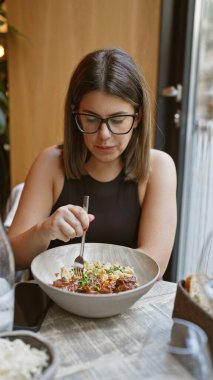 Genç İspanyol esmer kadın modern bir kafenin içinde gurme yemekleri yiyor.
