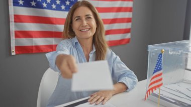 Gülümseyen bir Amerikalı kadın seçim kurulunda Amerikan bayrağının arka planına karşı bir sandığa oy veriyor..