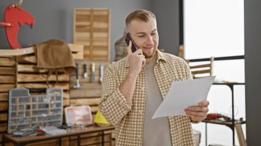 Ahşap atölyesinde telefonla konuşan yakışıklı beyaz adam bir belgeyi inceliyor..