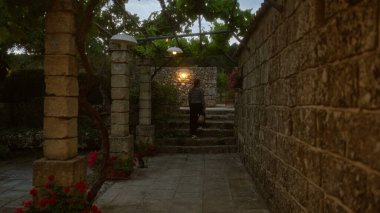 İtalya 'da bir kadın, alacakaranlıkta, yemyeşil ve çiçeklerle çevrili Puglia' daki resim gibi taş bir avluda yürüyor..