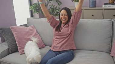 Neşeli bir kadın, sıcak bir oturma odasında köpeğinin yanında sevinçle uzanır..