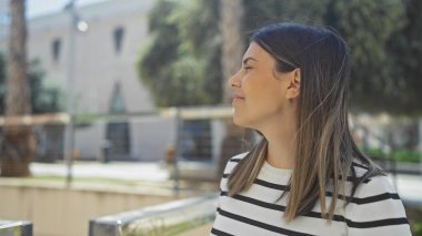 Çekici, çizgili tişörtlü esmer kadın şehir parkında güneşli bir günün tadını çıkarıyor..