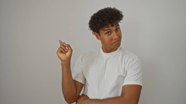 İzole edilmiş beyaz bir arkaplan üzerinde kendine güvenen bir yüz ifadesi olan genç bir adam, beyaz gömlek giyiyor..