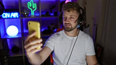 Yakışıklı, mavi gözlü adam gecenin karanlığında neon ışıklı oyun odasında selfie çekiyor..