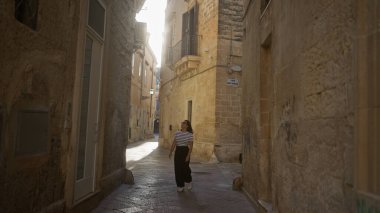 Dar taştan caddeleri keşfeden genç bir İspanyol kadın. Öğretim, puglia, İtalya. Gün ışığında..