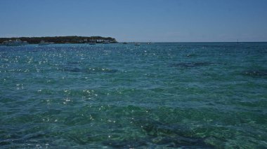 Porto cesareo's stunning turquoise waters in salento, puglia, italy, shimmer under the bright sun with boats dotting the distant horizon, creating an idyllic mediterranean seaside scene. clipart