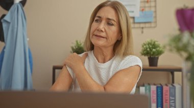 Rahat bir ofis ortamında omuz ağrısı çeken olgun bir kadın..