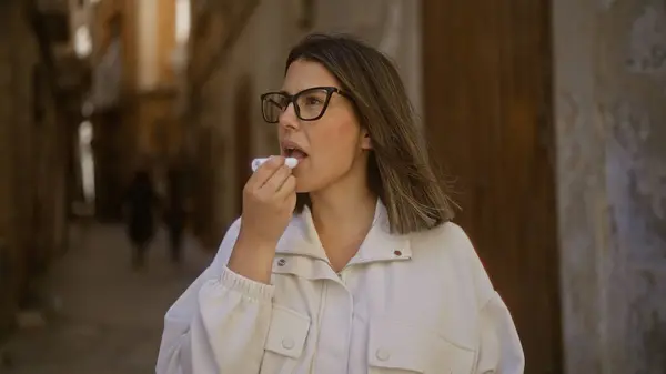 stock image A young, beautiful hispanic woman applies lip balm while strolling through the narrow streets of bari's old town in puglia, italy.