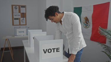Genç İspanyol bir adam, demokratik katılımı simgeleyen, Meksika bayrağıyla süslenmiş bir odada oy veriyor..