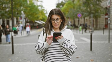 Hispanic woman using smartphone on budapest street clipart