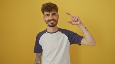 Dövmeleri ve sakalı olan yakışıklı genç bir adam parmaklarıyla küçük bir miktar jest yapar..