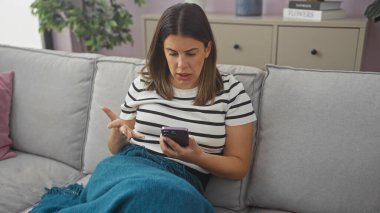 Kapalı bir koltukta oturan genç bir kadın kafası karışmış bir ifadeyle akıllı telefonuna bakıyor.