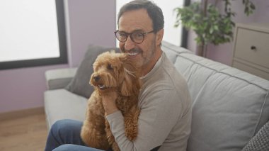 Sıcak bir oturma odasında kaniş tutan gülümseyen İspanyol bir adam olgun bir arkadaşlık ve evde rahatlık yayıyor..