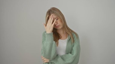 Yeşil kazaklı stresli genç bir kadın beyaz bir arka planda duruyor, elleri alnında, bunalmış görünüyor..