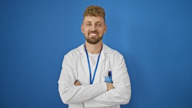 Mavi gözlü ve sakallı, laboratuvar önlüğü giymiş, mavi arka planda duran beyaz bir genç..