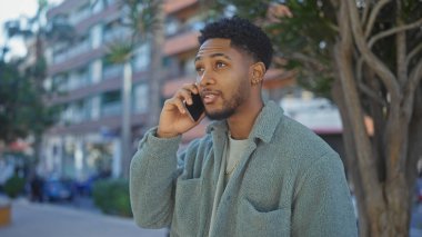 Afrika kökenli Amerikalı adam şehir manzarasında telefonla konuşuyor. Tarz ve bağlantı kuruyor..