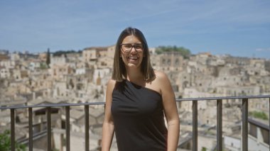 Genç bir İspanyol kadın, eski bir kasaba olan Mata, Basilicata, İtalya 'da, arka planda antik taş binalar ile berrak mavi bir gökyüzünün altında güzel bir gülümseme ile bir bakış açısında duruyor..