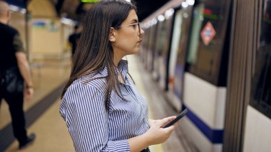 Madrid metro istasyonunda akıllı telefon kullanan güzel İspanyol bir kadın metroda bekliyor.