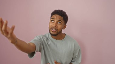 Afro-Amerikalı adam pembe bir duvara garip bir şekilde el kol hareketi yapıyor..