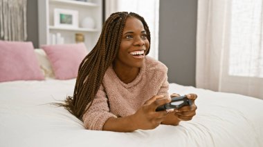Örgü örgülü Afrikalı Amerikalı kadın rahat bir yatak odasında oyun oynuyor, neşe ve keyif saçıyor..