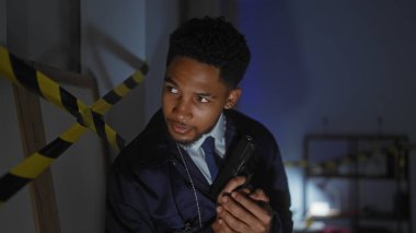 Afrika kökenli Amerikalı bir adam, dedektif rolünde, tetikte ve ihtiyatlı, loş bir odada, uyarı bandıyla işaretlenmiş bir silahla..