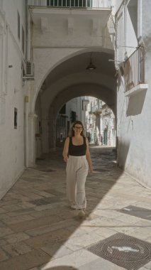 Genç bir İspanyol kadın Puglia, İtalya 'da yaşlı bir kasabanın resimli sokaklarında yürüyor taş sokaklar ve kemerlerle güzel mimariyi aydınlatıyor..