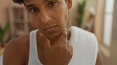 Sağlık merkezinde boynu havluyla gezen genç bir adam ve derin düşüncelere dalmış bir ifade.