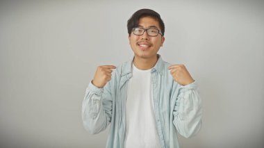 Beyaz bir duvara karşı kot ceketli, beyaz tişörtlü, kendini gösteren neşeli Asyalı bir adam..