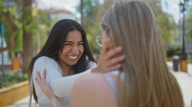 Güneşli bir şehir parkında neşeyle gülen iki kadın, açık hava ortamında dostluk ve mutluluk tasvir ediyorlar..