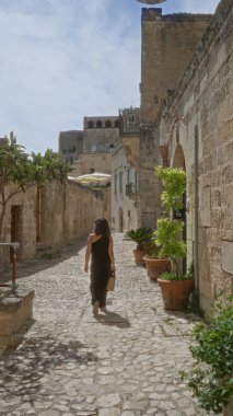 Güzel, genç bir İspanyol kadın, tarihi taş binalar ve açık mavi gökyüzünün altındaki yemyeşil saksı bitkilerle çevrili İtalya 'nın Basilicata kentindeki büyüleyici eski anne kasabasında yürüyor..