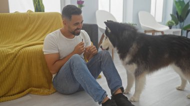 Yakışıklı İspanyol erkeği, sadık köpeğiyle sıcak, modern bir oturma odasında kaliteli zaman geçiriyor..