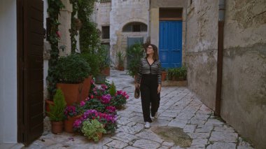 Genç İspanyol bir kadın polignano 'nun büyüleyici, çiçek desenli sokaklarında yürüyor. Bir kısrak, puglia, İtalya, günlük kıyafetler giyip Avrupa mimarisinin tadını çıkarıyor..
