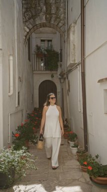 Beyazlar içindeki genç ve güzel İspanyol bir kadın. Locorotondo 'nun büyüleyici dar sokaklarında yürüyor. Puglia, İtalya' da eski bir kasaba..