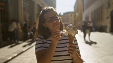 Genç bir İspanyol kadın güneşli bir günde güneşli bir günde dondurma yiyor. Lezzetli bir şehir manzarasının özünü yakalıyor..