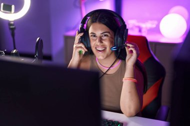 Young beautiful hispanic woman streamer playing video game using computer at gaming room