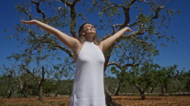 Beyaz elbiseli, güzel, genç bir İspanyol kadın Puglia, İtalya 'da açık mavi bir gökyüzünün altında kollarını açmış, neşeli bir şekilde ayakta duruyor..